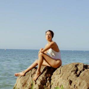 Femme en maillot de bain assise au bord de la mer sur des rochers